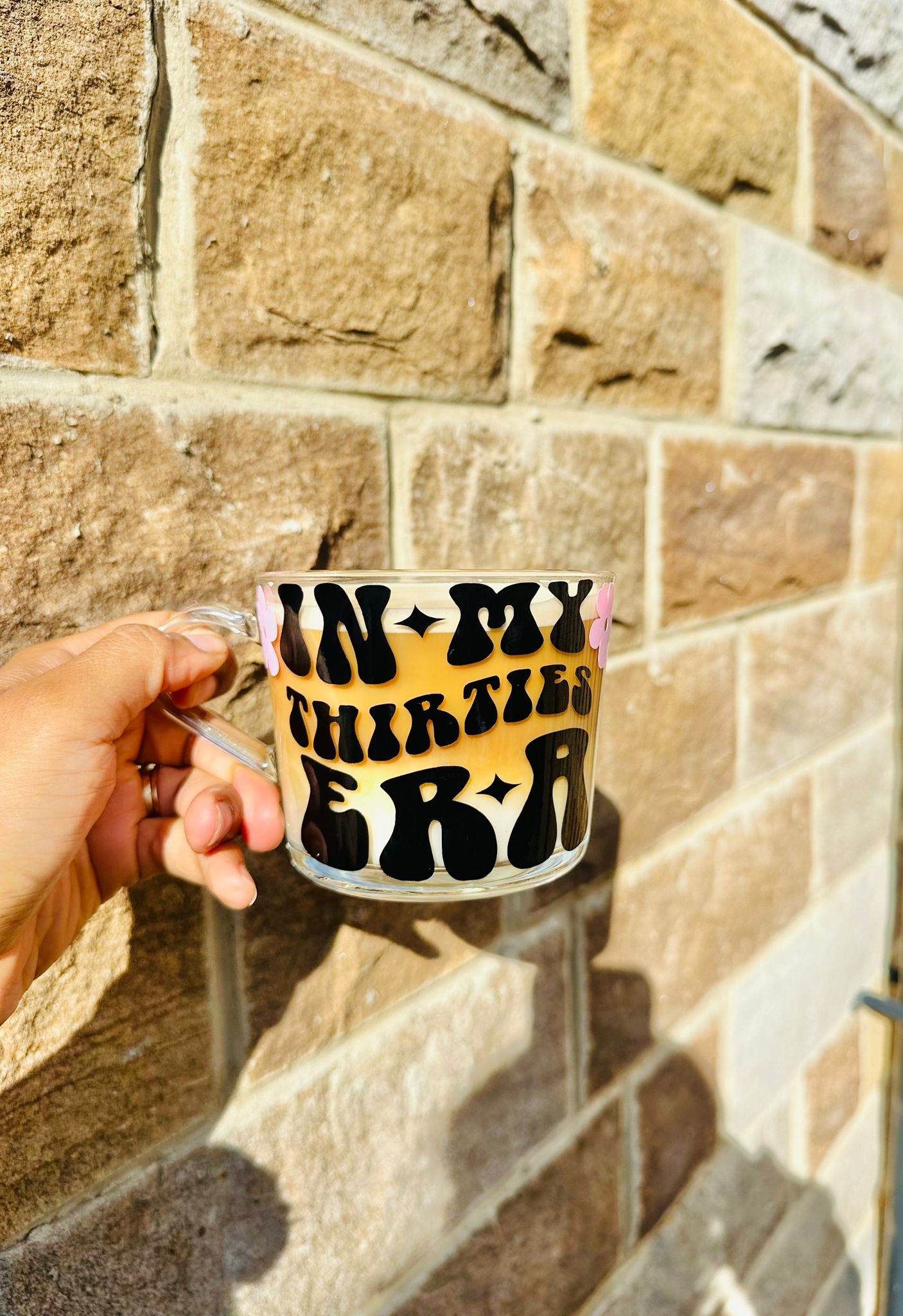 A glass mug featuring the text in my thirties era. It features a glass with coffee inside it.